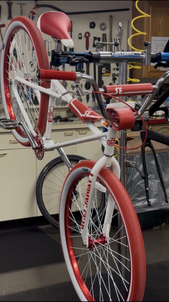 Red and white SE bike mounted on a repair stand inside Bicycles Plus